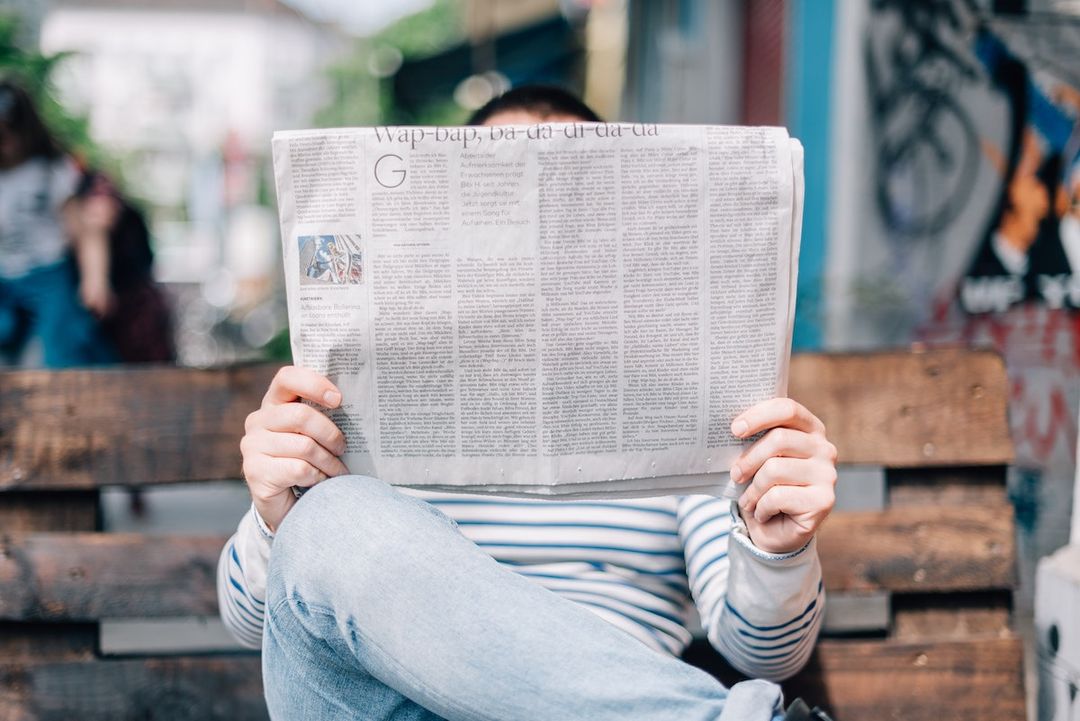 A person reading a broadsheet newspaper outdoors